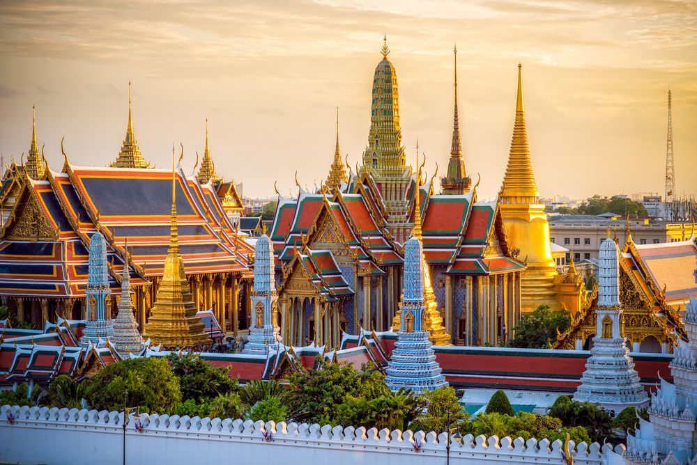 Golden spires and colorful roofs of Wat Phra Kaew and Grand Palace in Bangkok, Thailand during sunset