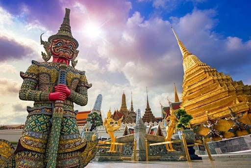 Majestic Yaksha demon guardian statue and golden chedi spire inside the Grand Palace complex in Bangkok Thailand