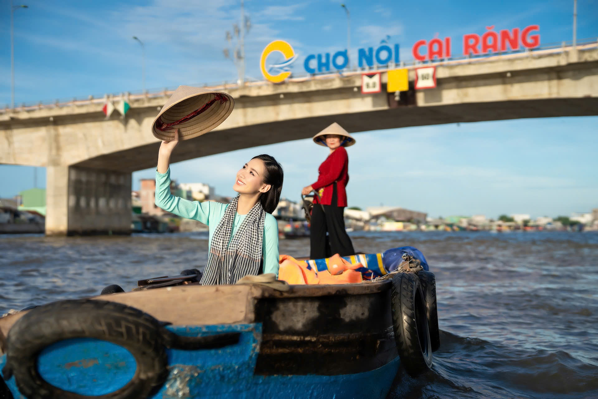 Traveler posing on a wooden sampan in front of Cai Rang floating market bridge