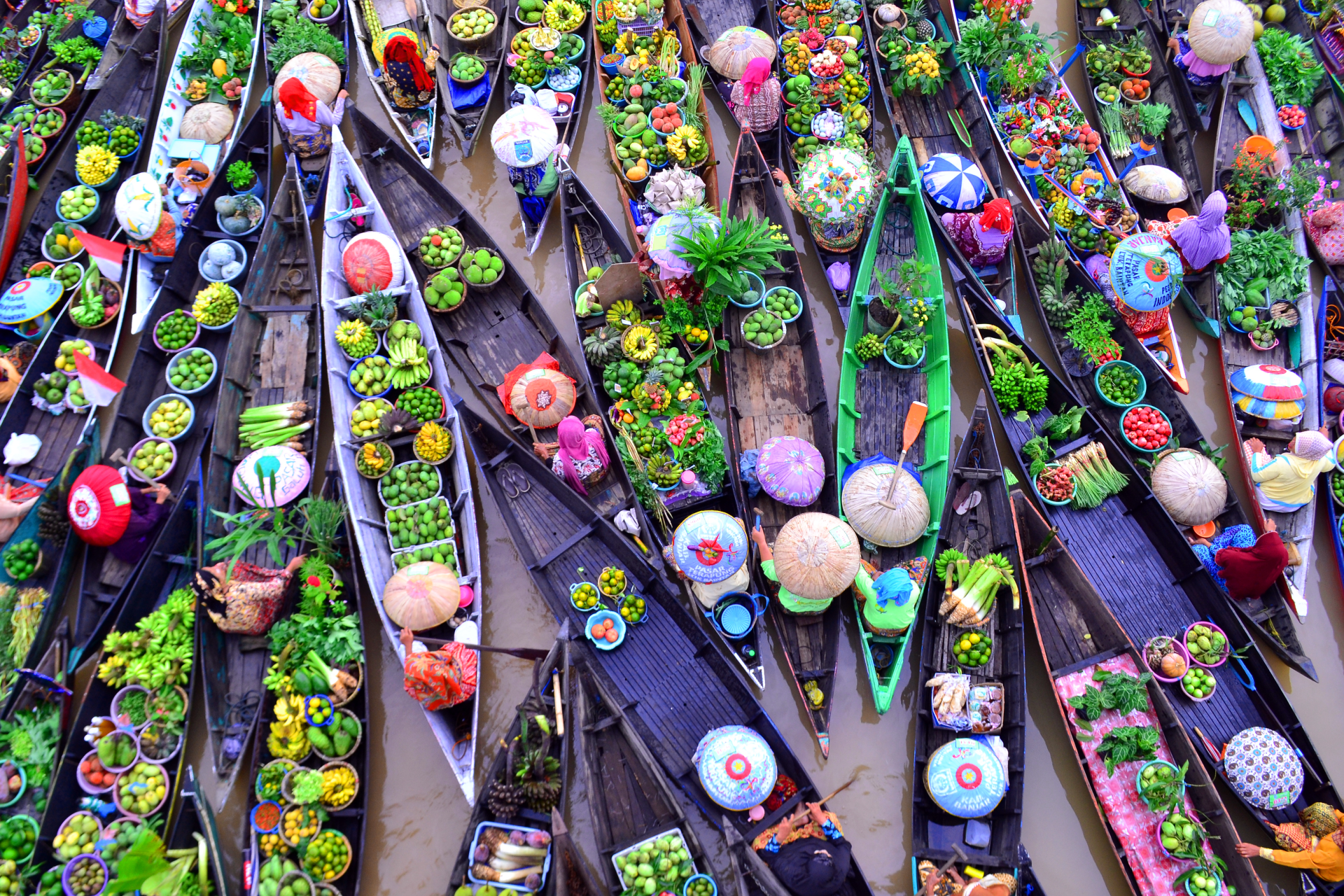 An overhead view of a colorful floating market, featuring crowded wooden boats laden with fresh fruit and vendors wearing conical hats