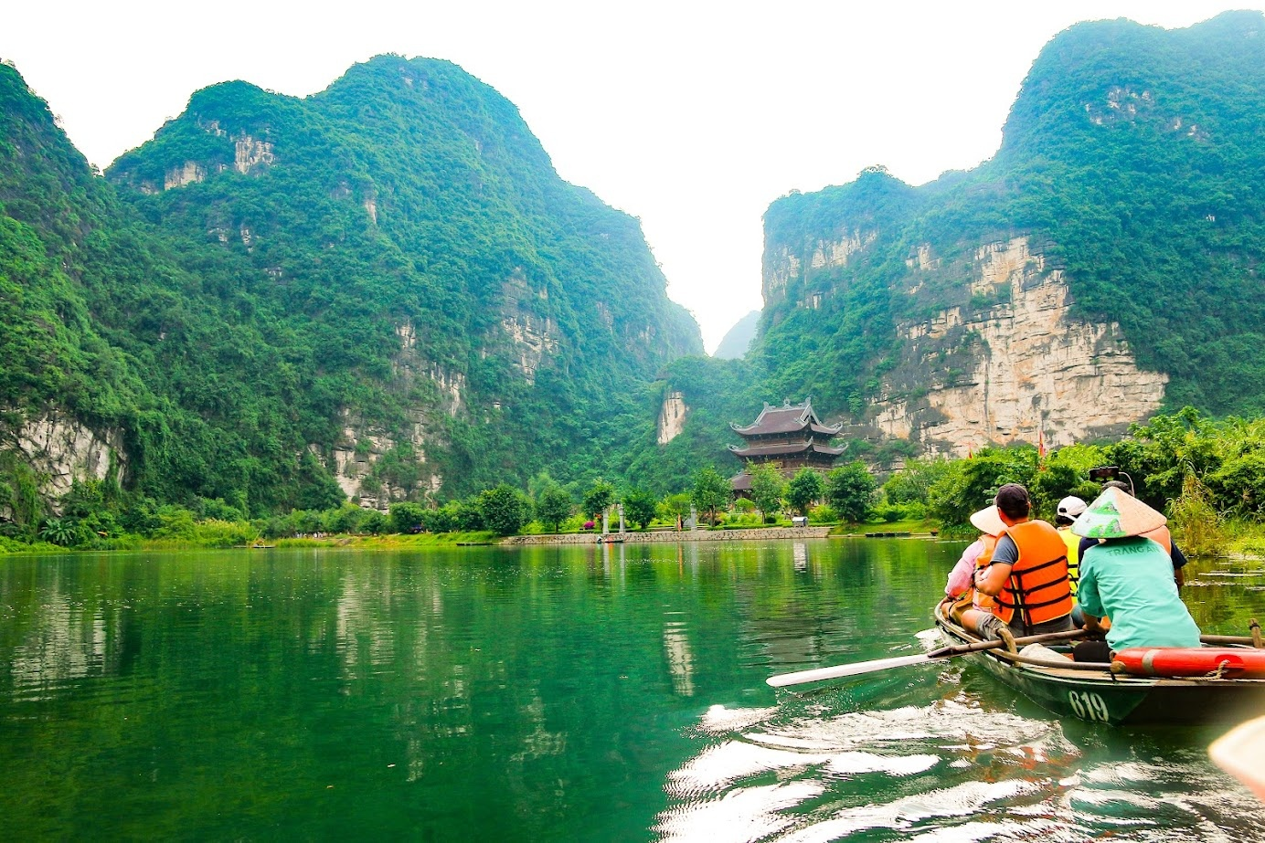Traditional wooden boat cruising through emerald water and karst mountains in Trang An Ninh Binh