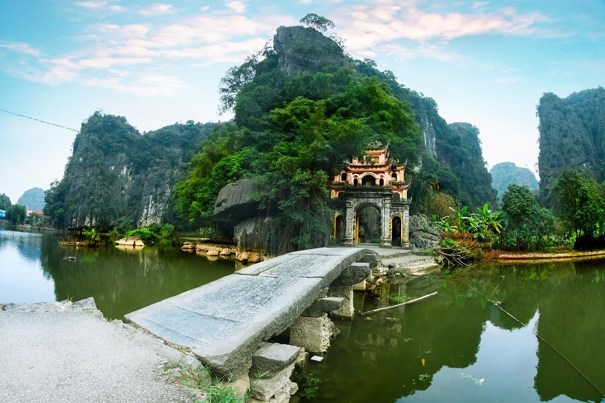 Ancient stone bridge and arched gate of Bich Dong Pagoda against limestone cliffs in Ninh Binh