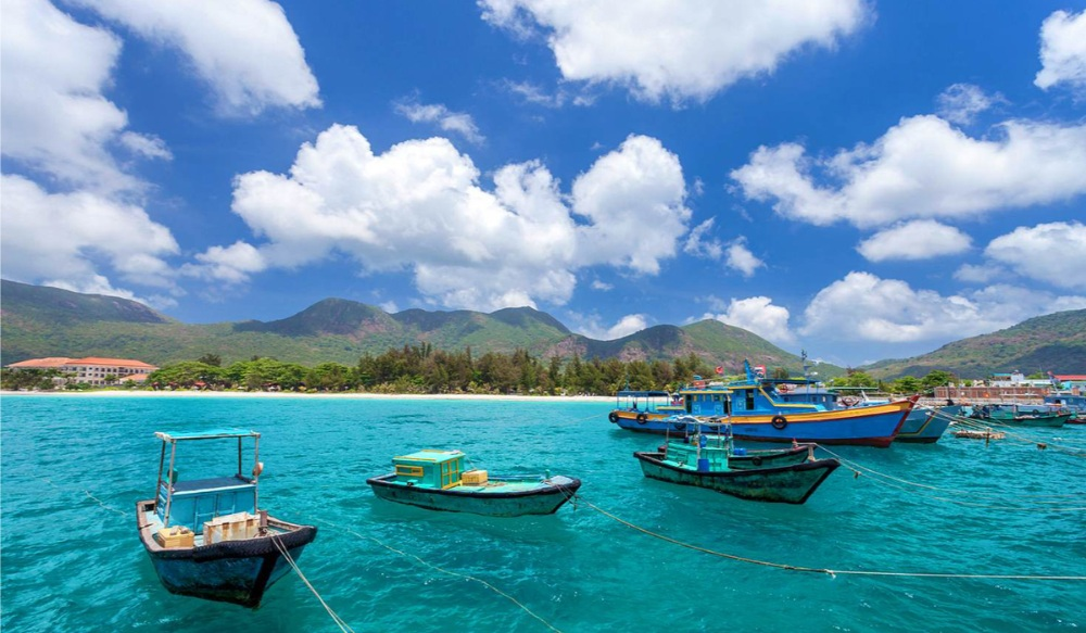 Wooden fishing boats anchored in clear turquoise sea water with green hills in the background at Con Dao Island, Vietnam