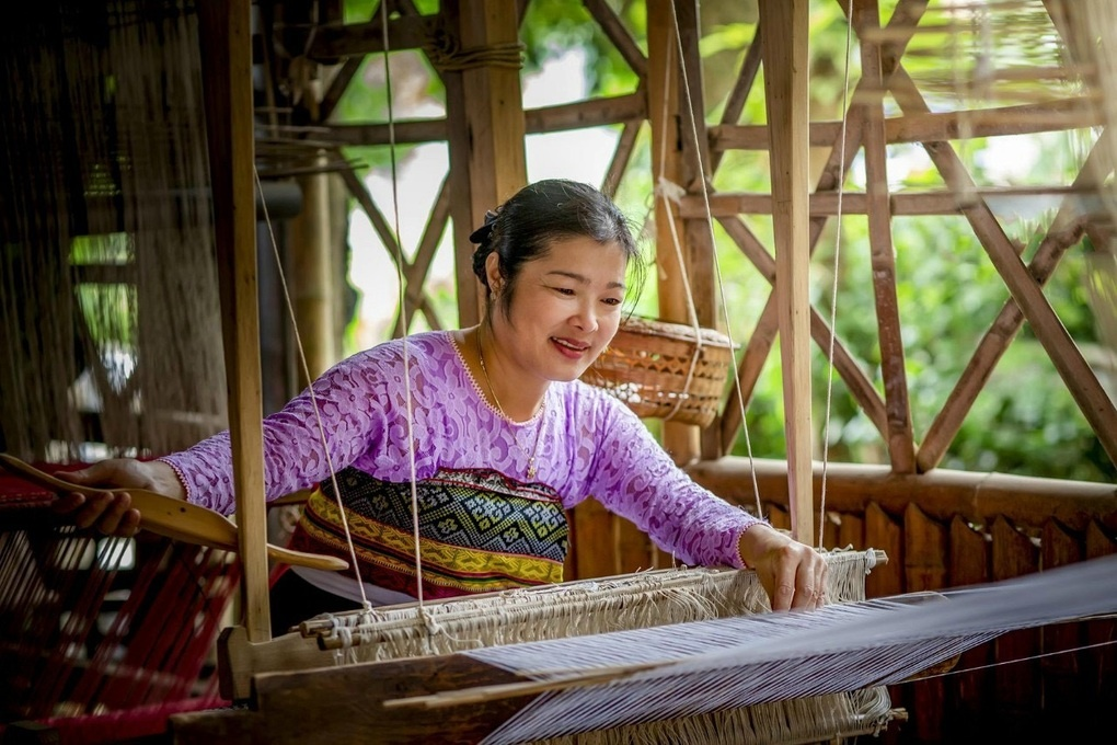 Local White Thai woman weaving traditional brocade fabric on a wooden loom